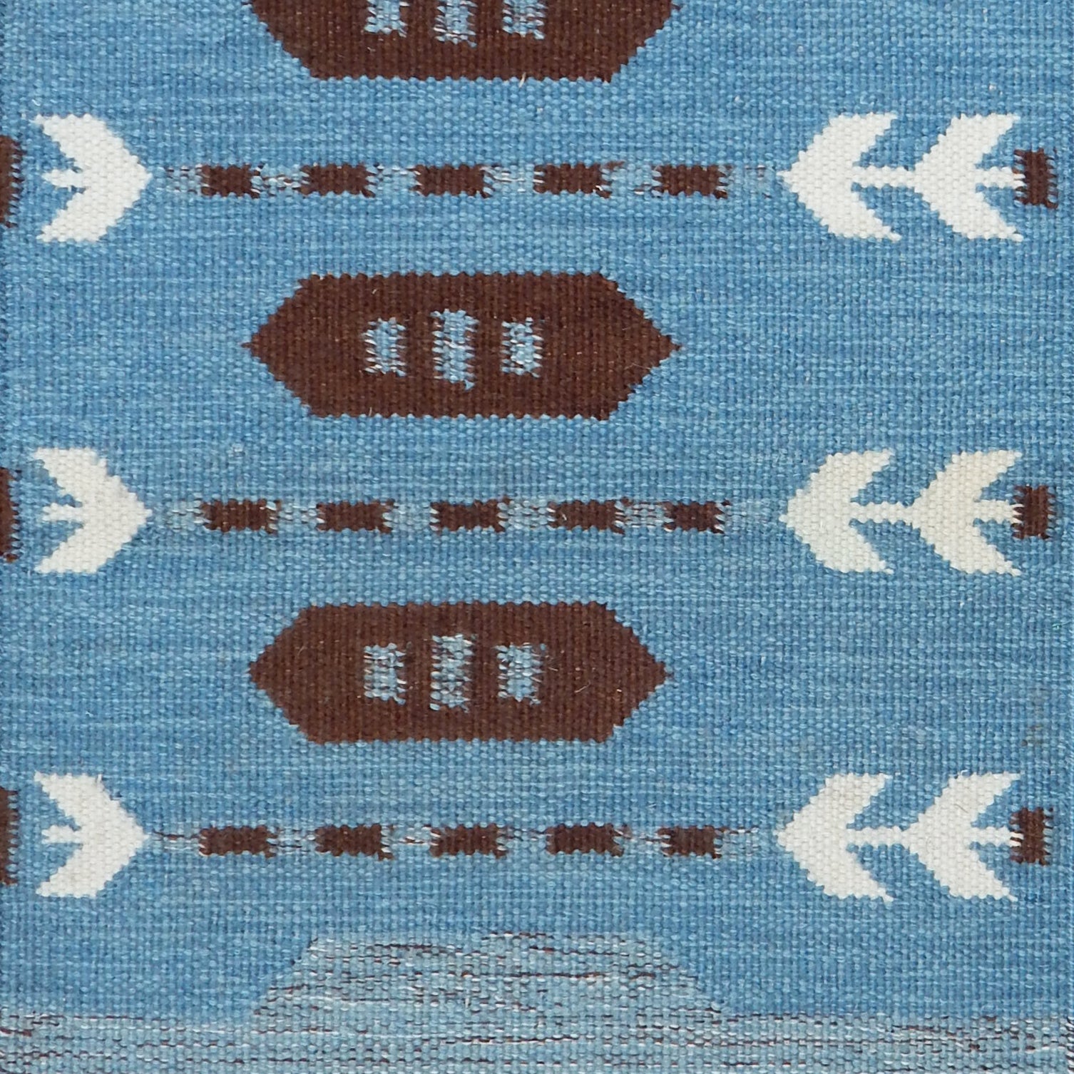 Handwoven rug detail in a Swedish arrow design in brown and white on a green field. 