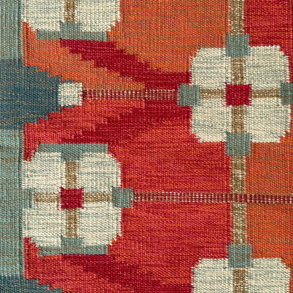 Handwoven rug detail in a Swedish Floral Trellis design in white and teal on an orange and red field