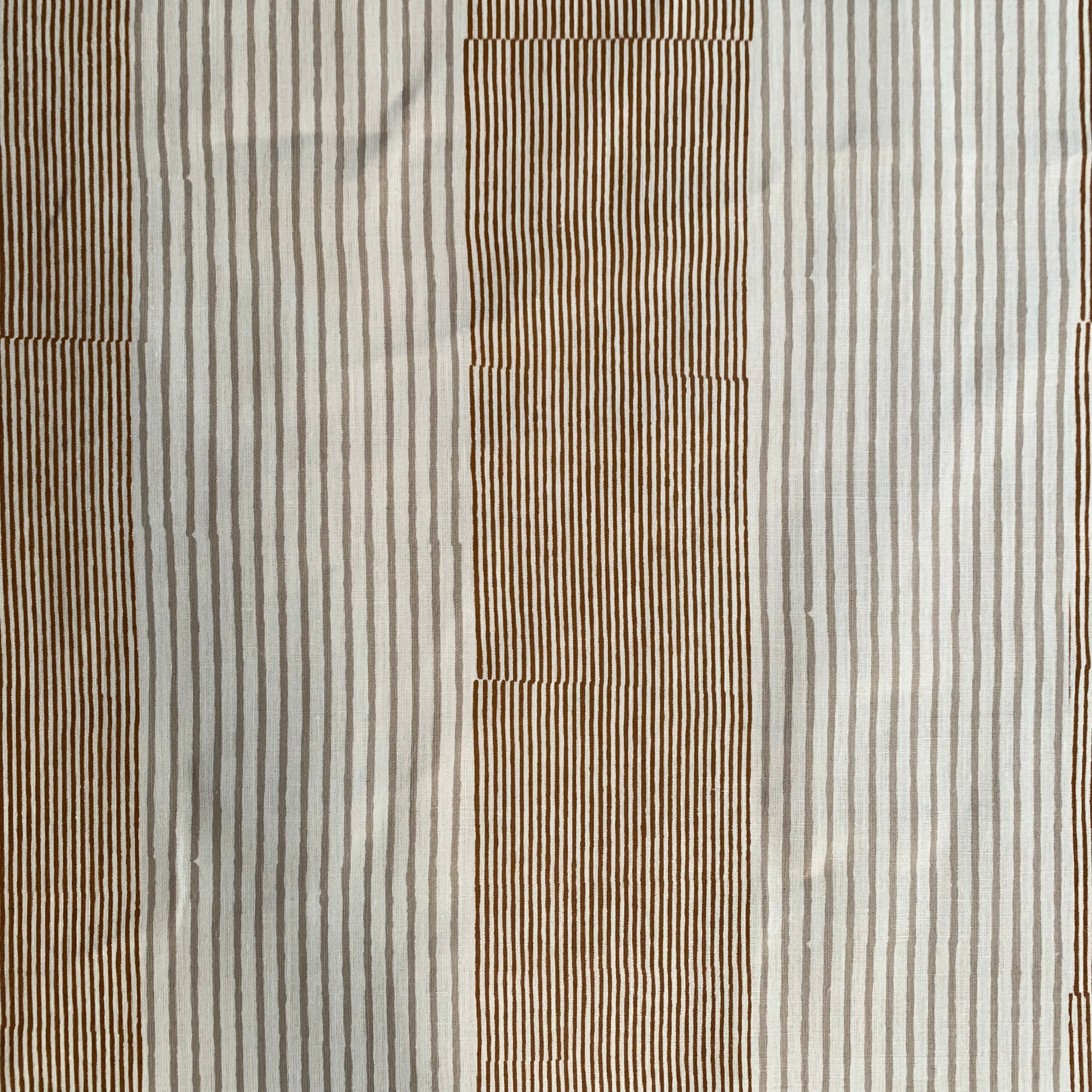 Detail of fabric in an irregular stripe print in rust and tan on a white field.