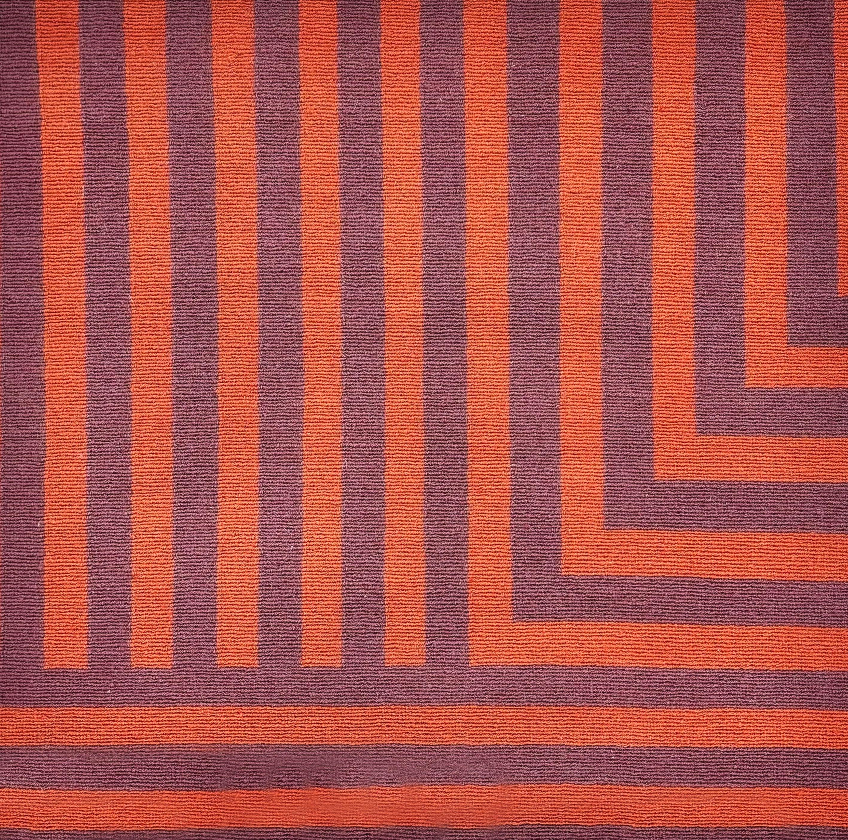 Detail of a handknotted rug in a graphic geometric design in red and eggplant purple.