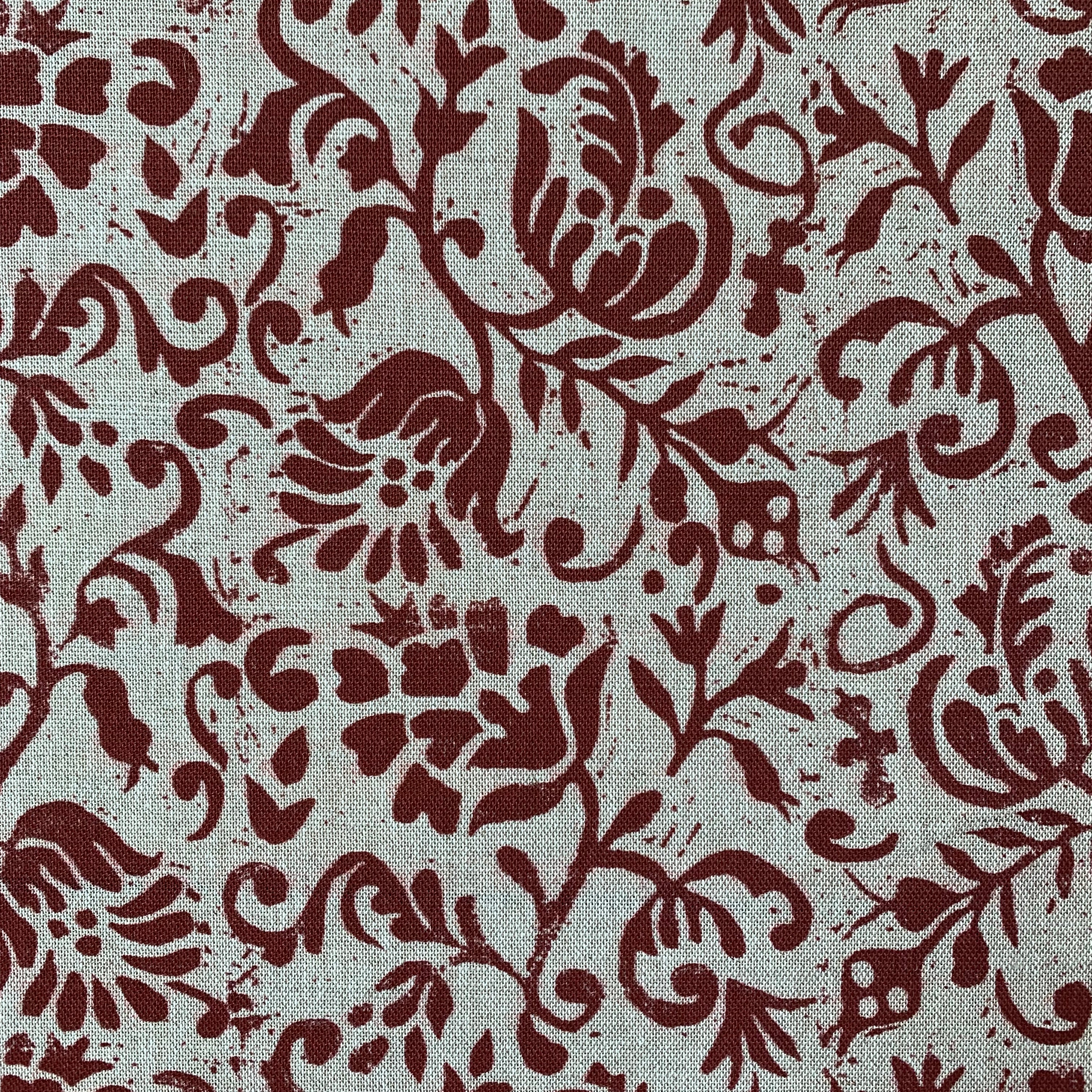 Close-up of fabric in a botanical print in red on a cream field.