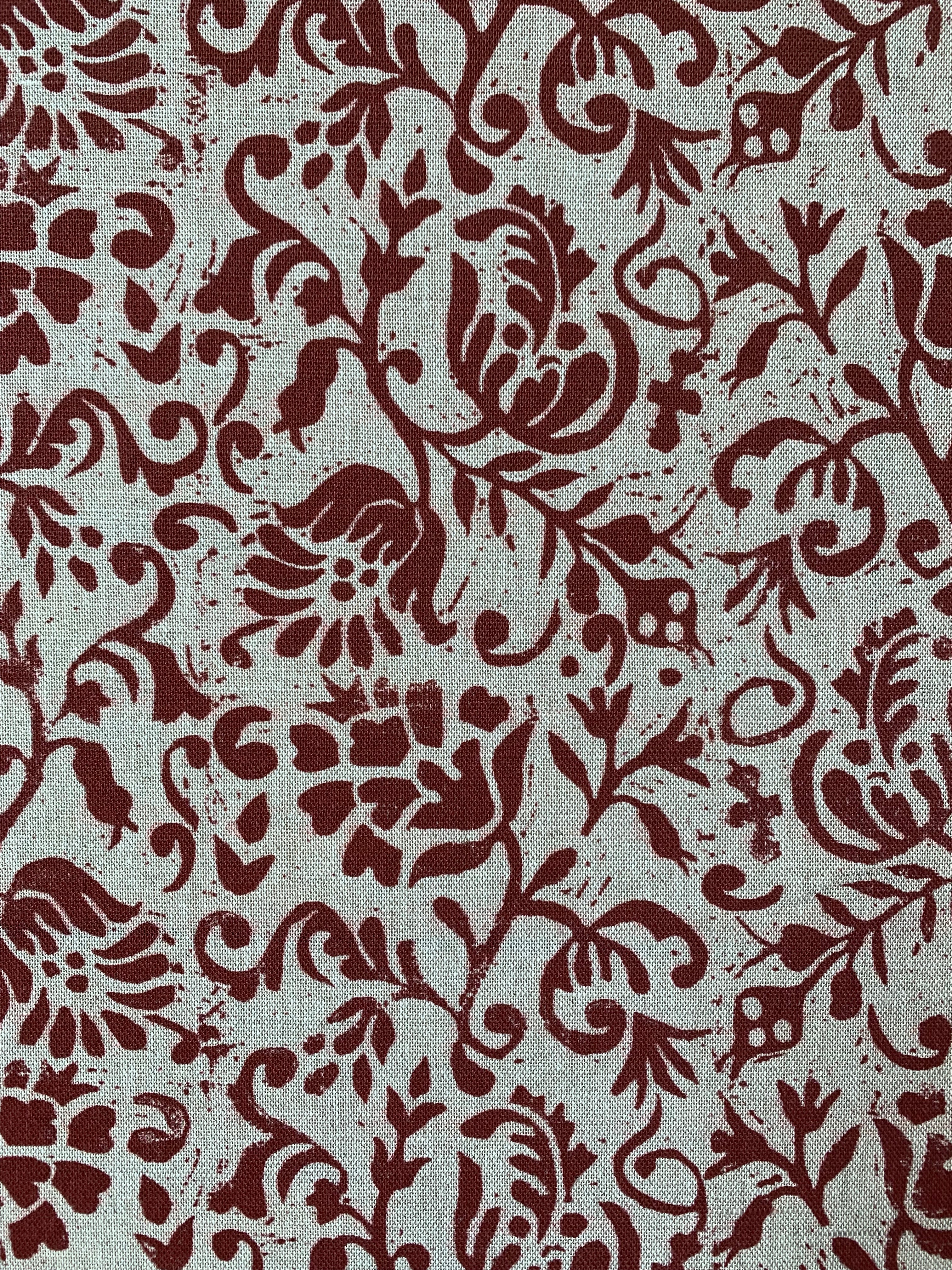 Close-up of fabric in a botanical print in red on a cream field.