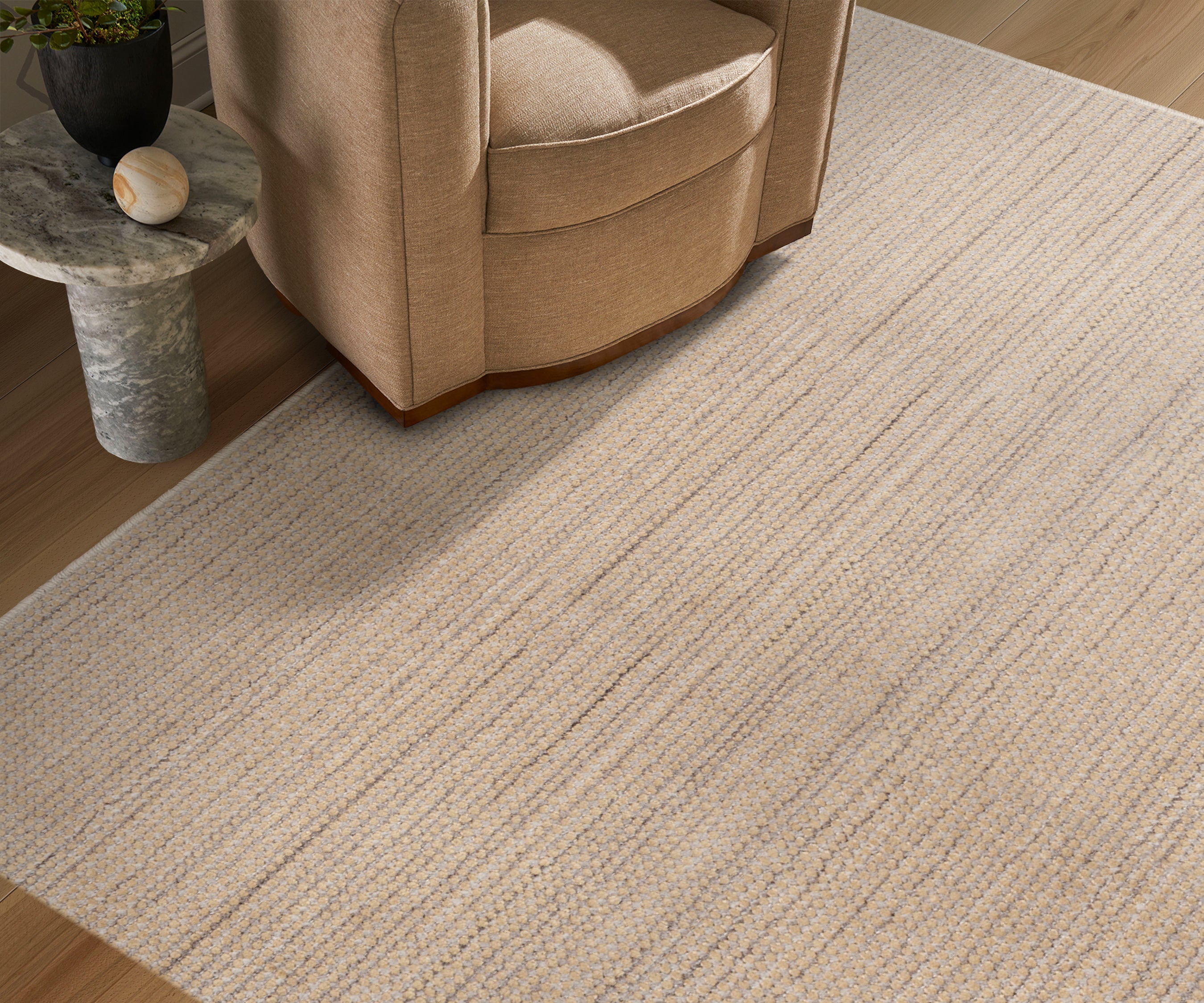 Beige armchair next to a textured beige rug on a wooden floor.