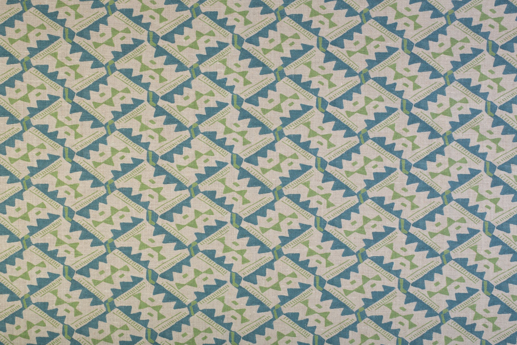 Detail of fabric in painterly diamond print in blue and green on a white field.