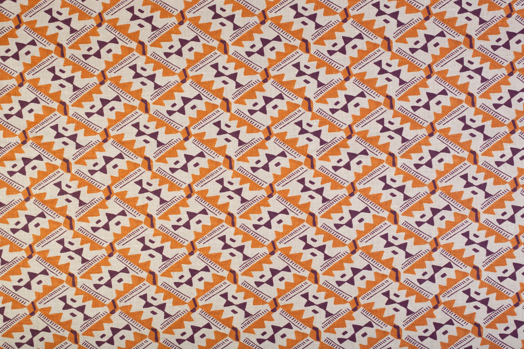 Detail of fabric in painterly diamond print in maroon and orange on a white field.