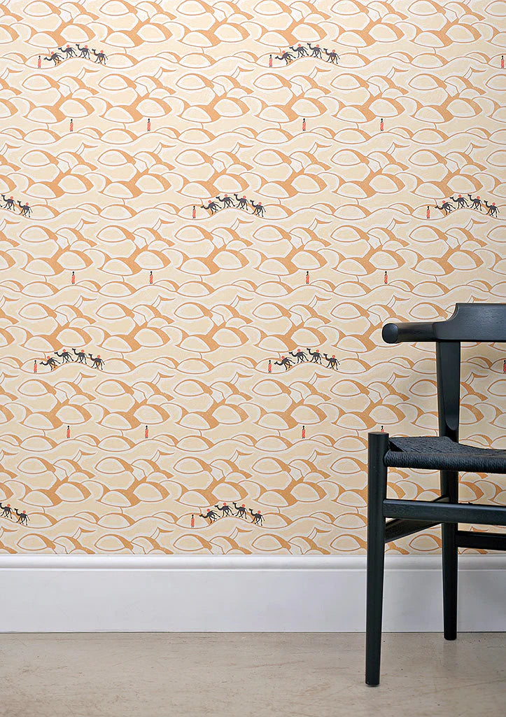 A black chair stands in front of a wall papered in a playful sand dune and camel print in orange, yellow and black.