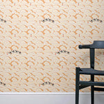 A black chair stands in front of a wall papered in a playful sand dune and camel print in orange, yellow and black.