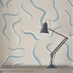 A desk lamp stands in front of a wall papered in a painterly botanical print in blue, white and tan.
