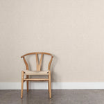 A wooden chair stands in front of a wall papered in a small-scale grid pattern in shades of cream.