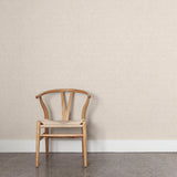 A wooden chair stands in front of a wall papered in a small-scale grid pattern in shades of cream.