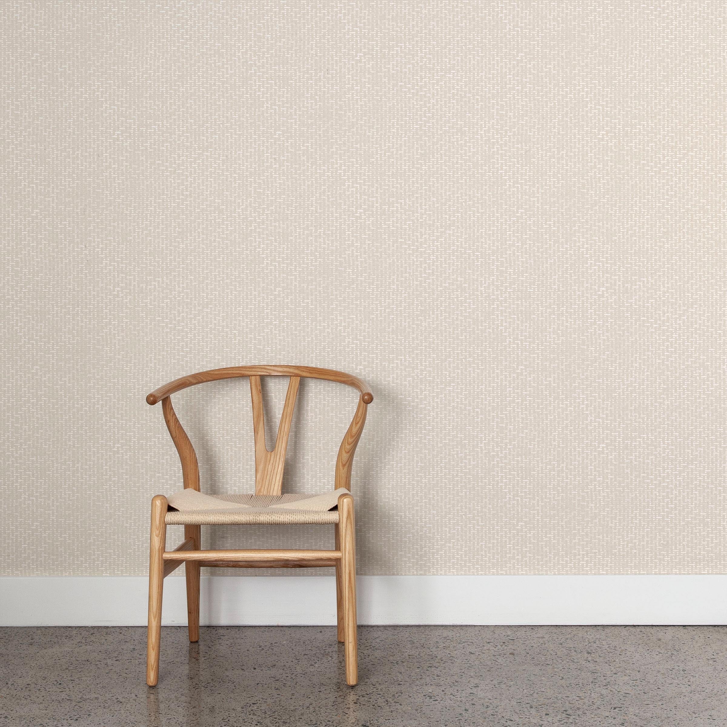 A wooden chair stands in front of a wall papered in a small-scale grid pattern in shades of cream.