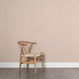 A wooden chair stands in front of a wall papered in a small-scale grid pattern in shades of pale pink.