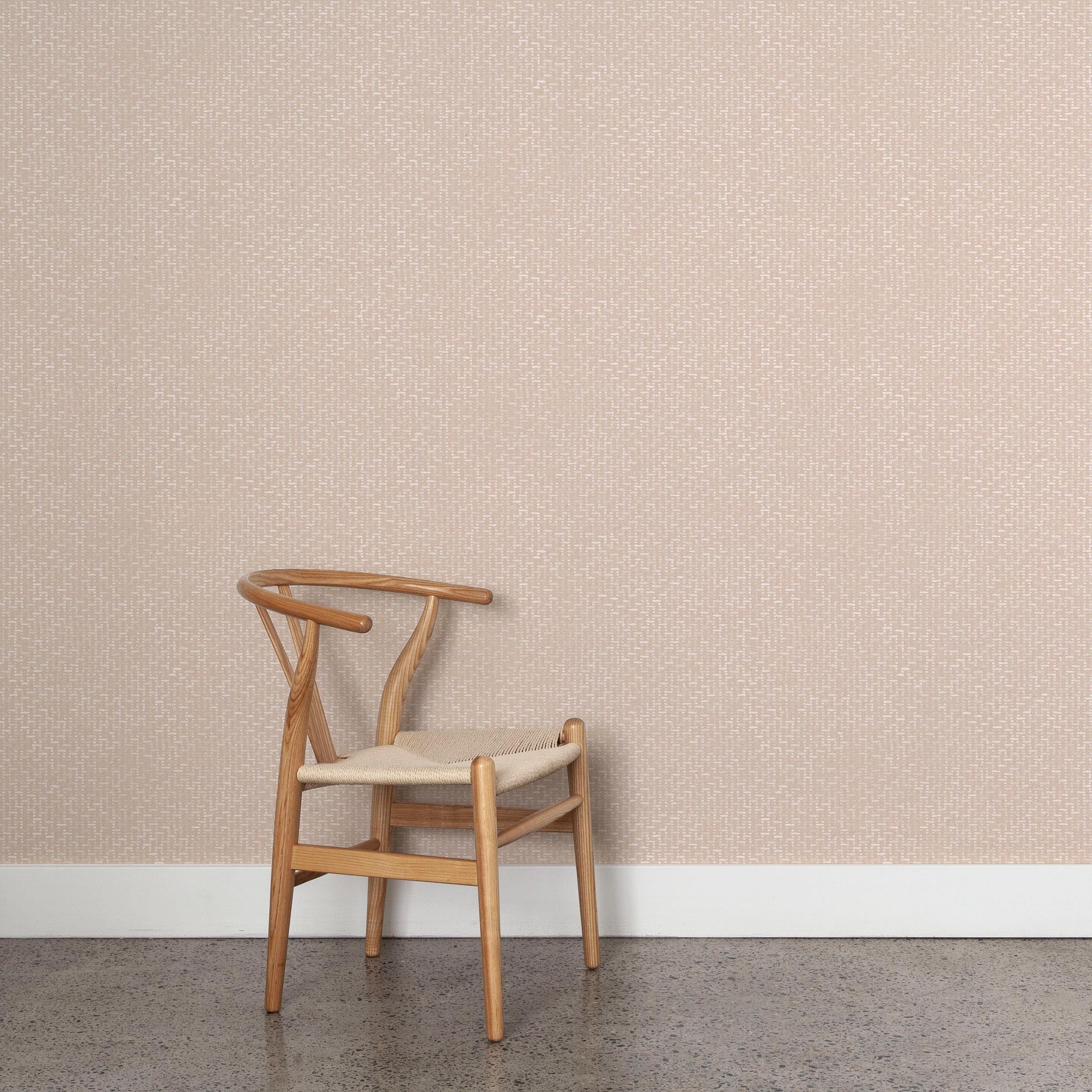 A wooden chair stands in front of a wall papered in a small-scale grid pattern in shades of pale pink.