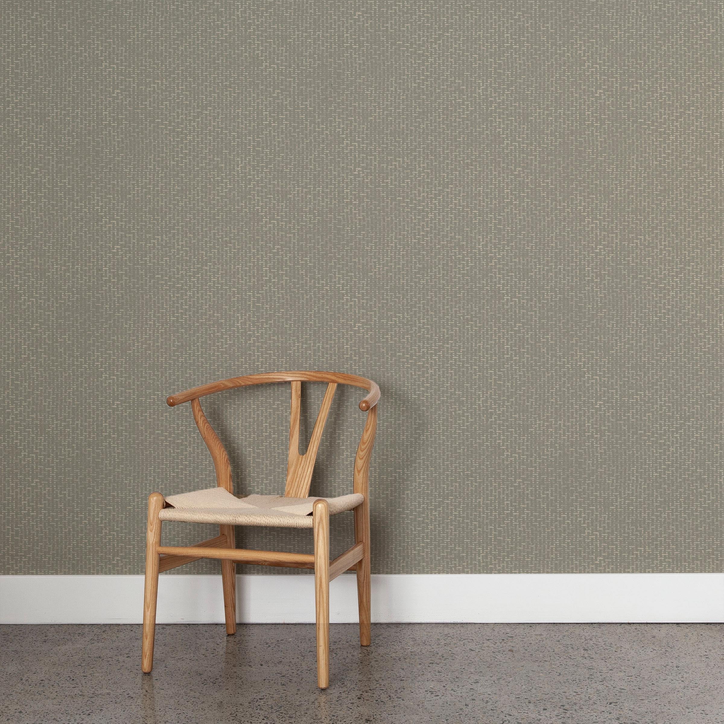 A wooden chair stands in front of a wall papered in a small-scale grid pattern in shades of gray.