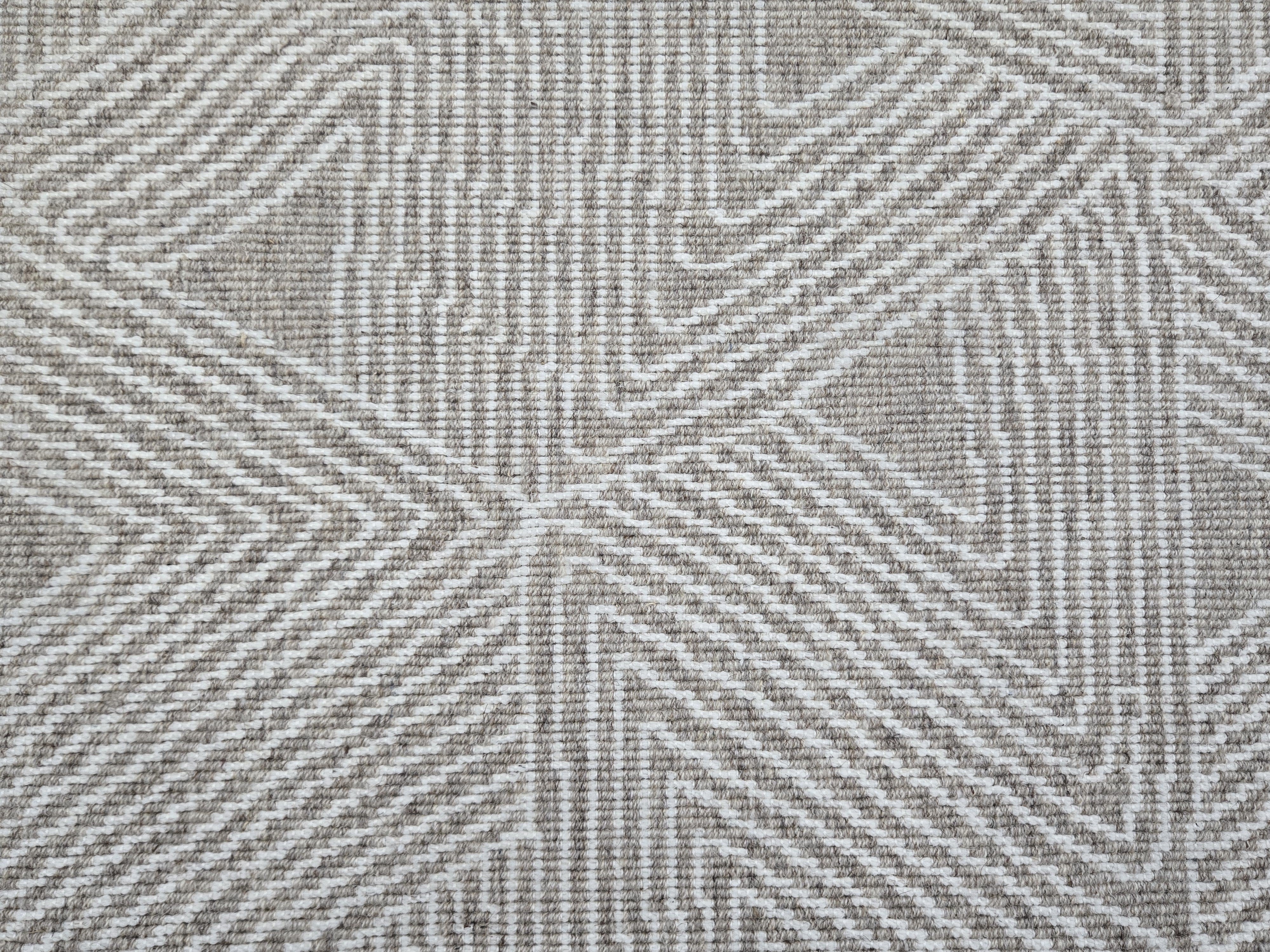 Broadloom carpet sample in a geometric linear pattern in cream on a tan field. 