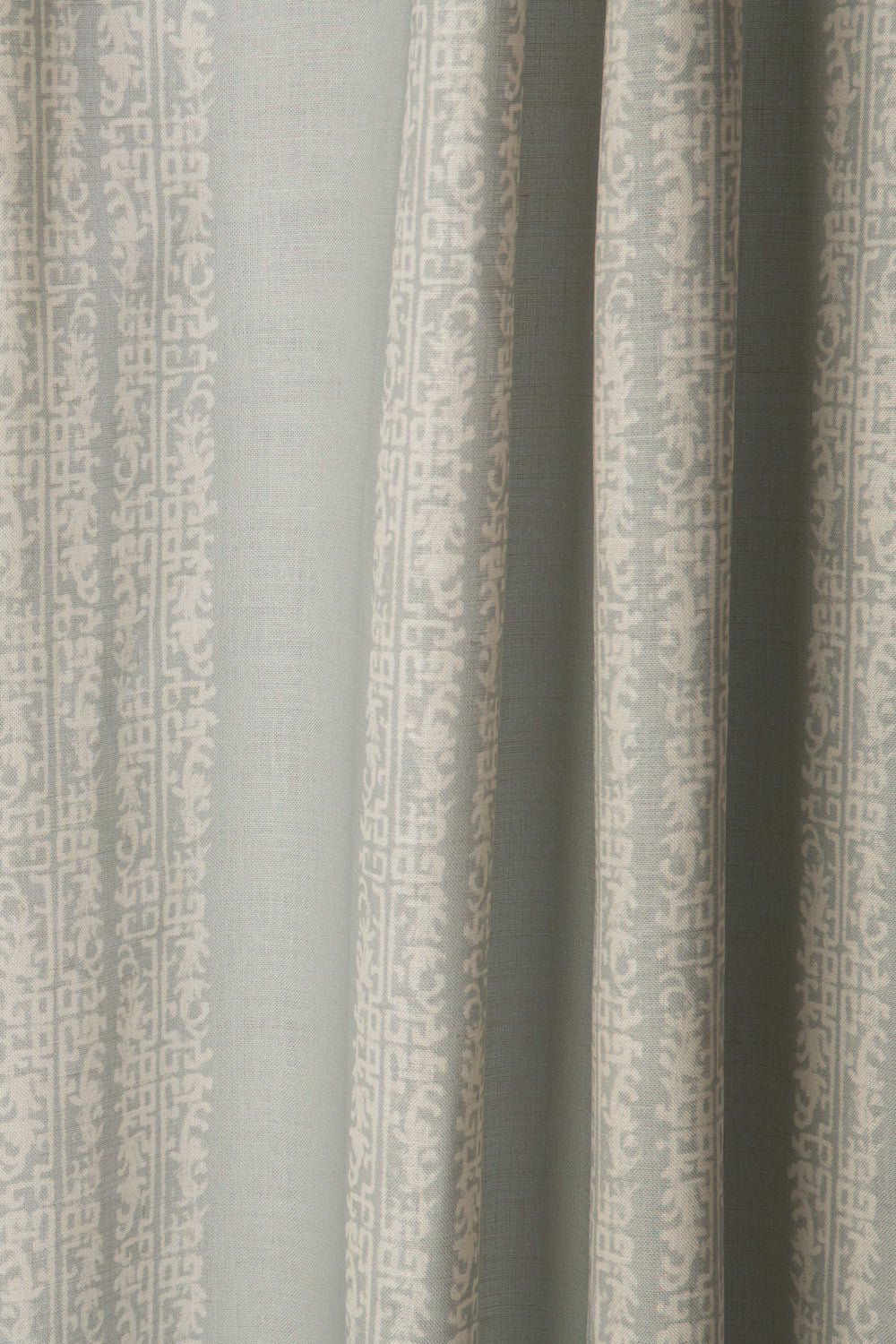 Draped printed fabric in a scrolling floral stripe pattern in cream on a light blue-gray field.