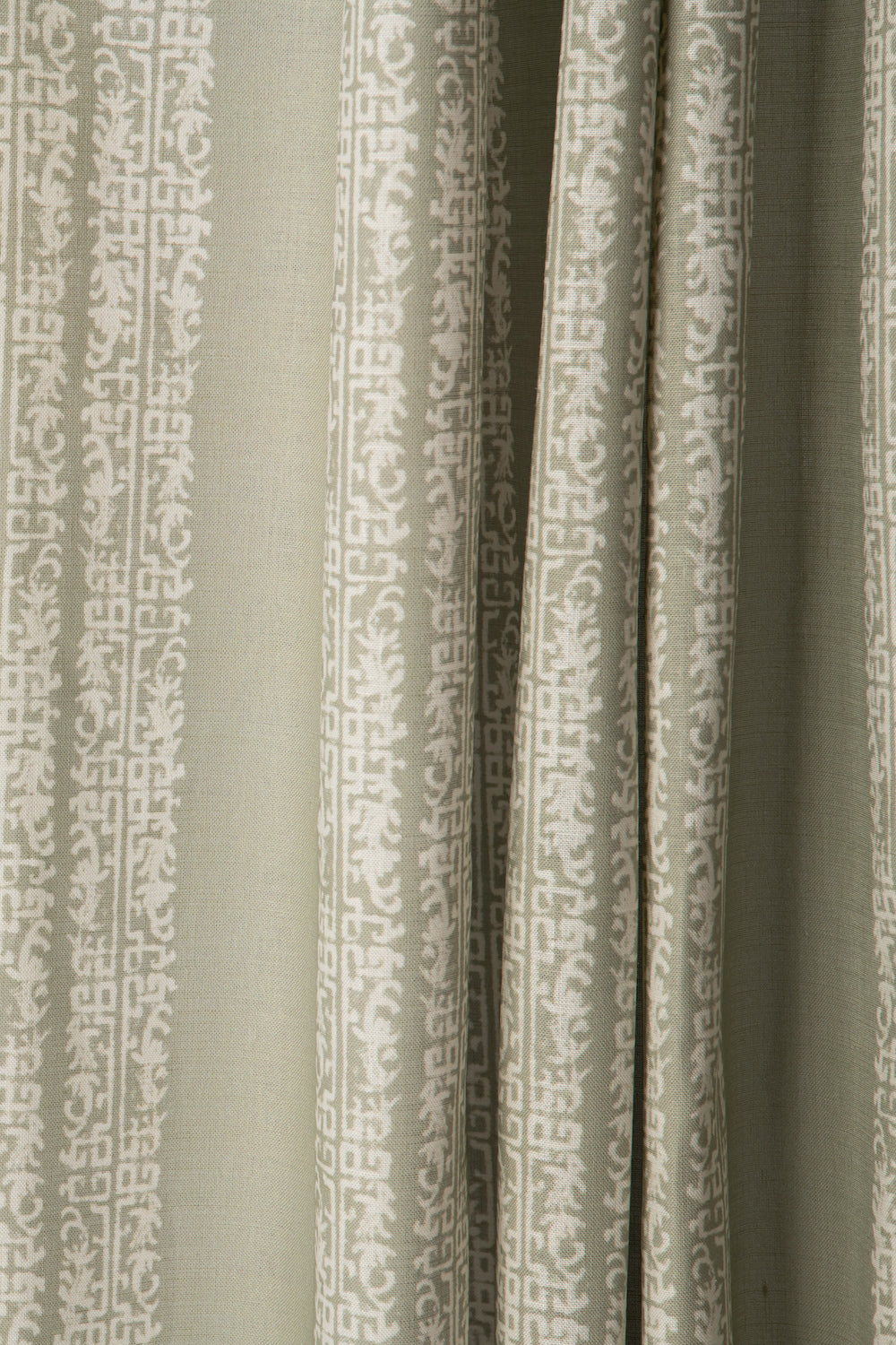 Draped printed fabric in a scrolling floral stripe pattern in cream on a light sage field.