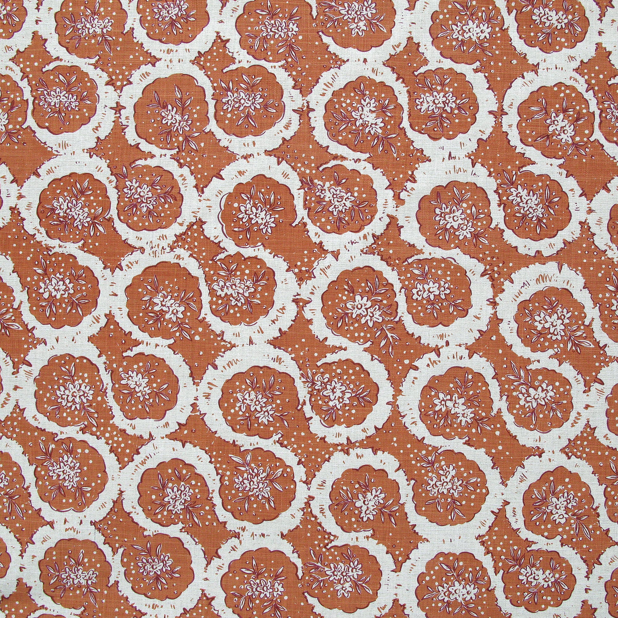 Detail of fabric in a meandering floral grid print in white and maroon on a burnt orange field.