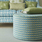 An ottoman and sofa covered in throw pillows, both upholstered in coordinating blue and green printed fabrics.