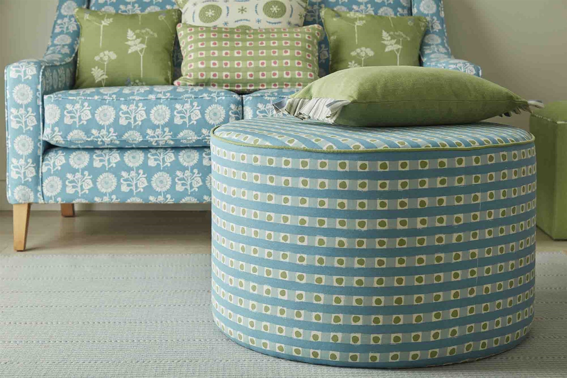 An ottoman and sofa covered in throw pillows, both upholstered in coordinating blue and green printed fabrics.