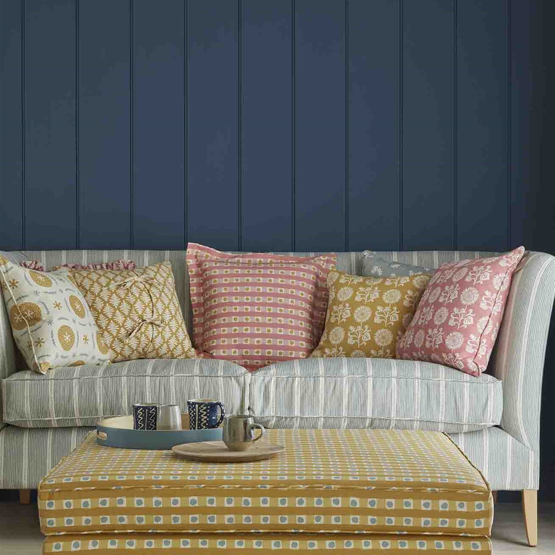 An ottoman and sofa covered in throw pillows, both upholstered in coordinating blue and mustard printed fabrics.