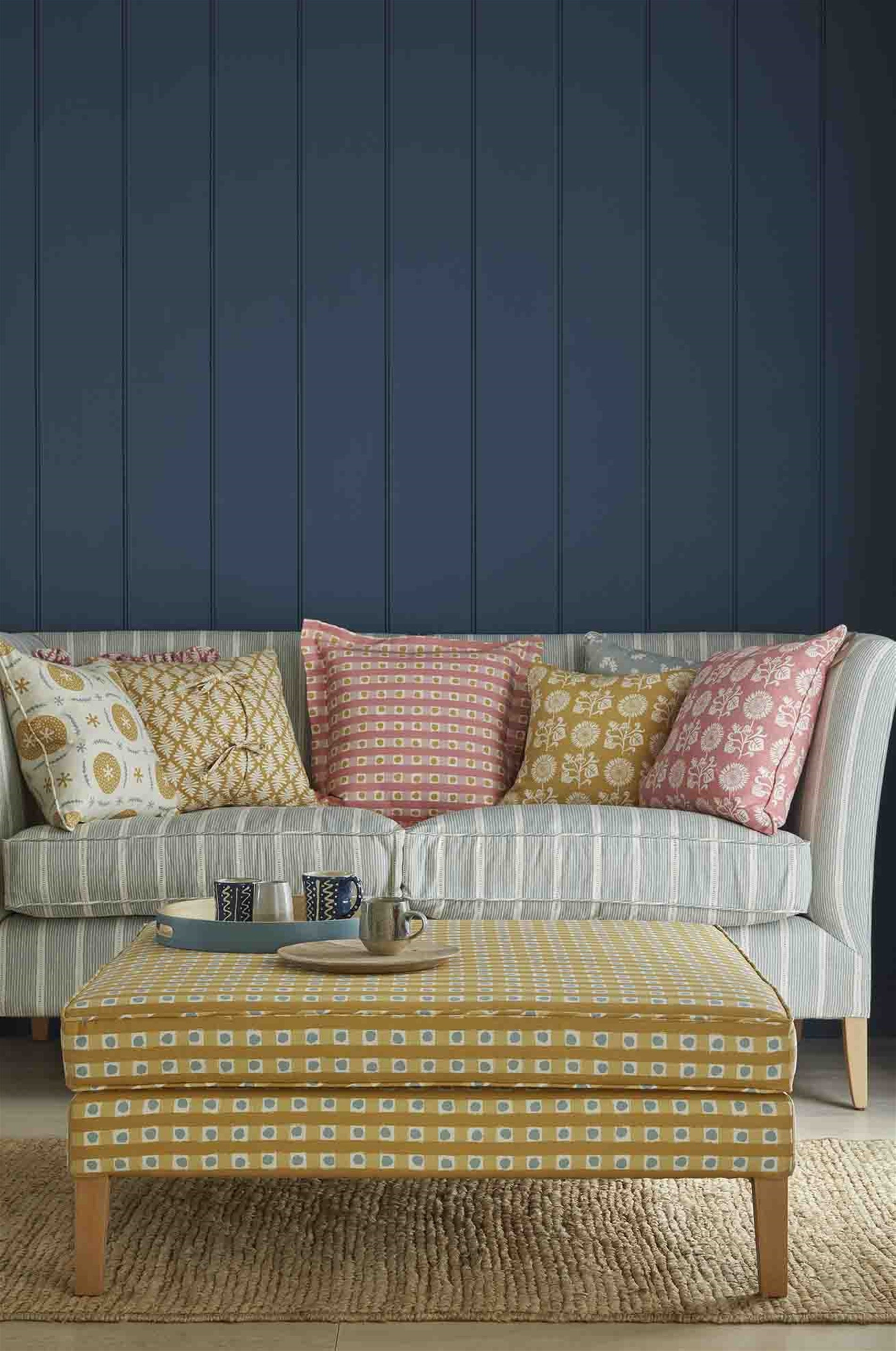 An ottoman and sofa covered in throw pillows, both upholstered in coordinating blue and mustard printed fabrics.