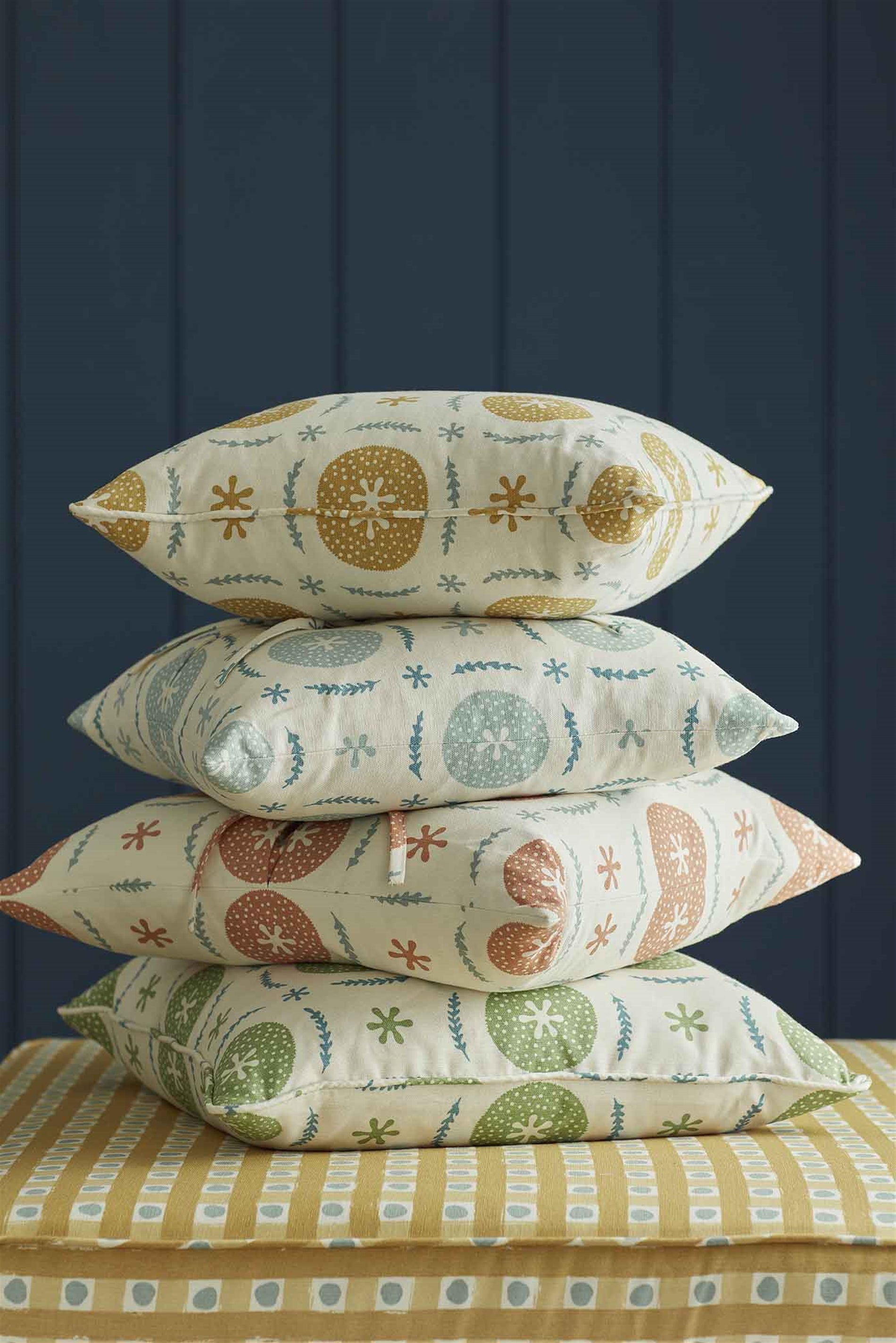 A stack of throw pillows in different colorways of the same playful berry and leaf print.