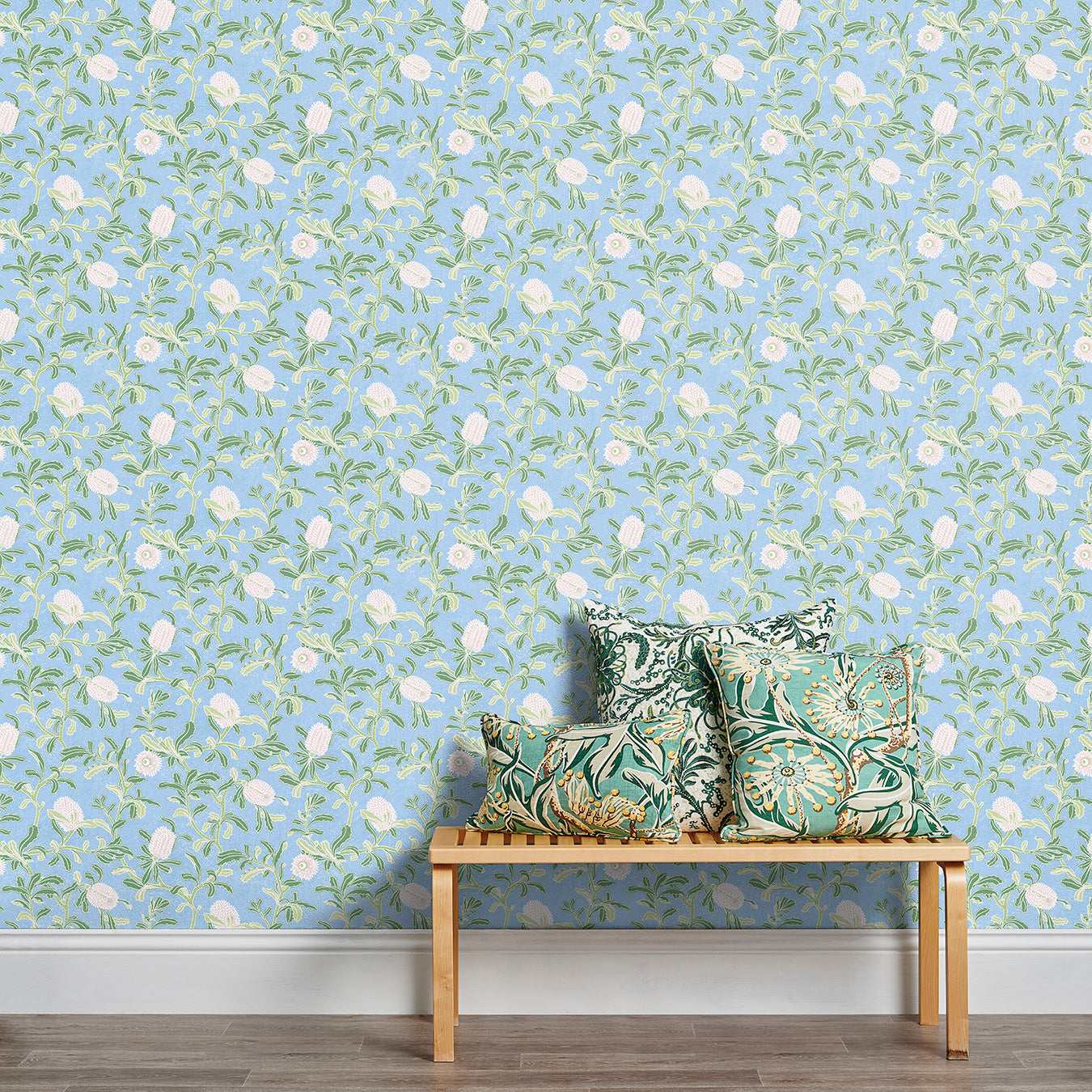 A stool stacked with throw pillows in front of a wall papered in a floral print in white, green and blue.