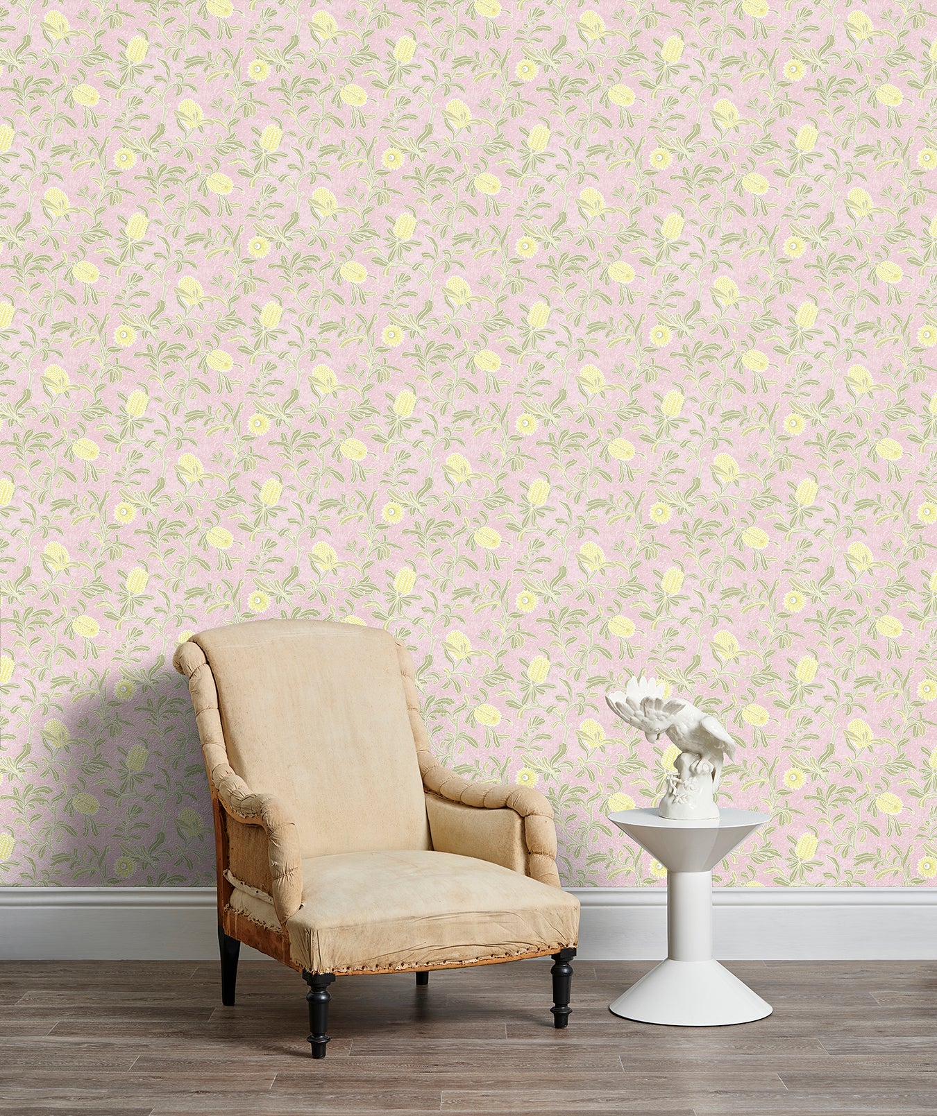 Armchair and end table in front of a wall papered in a floral print in yellow, green and light pink.