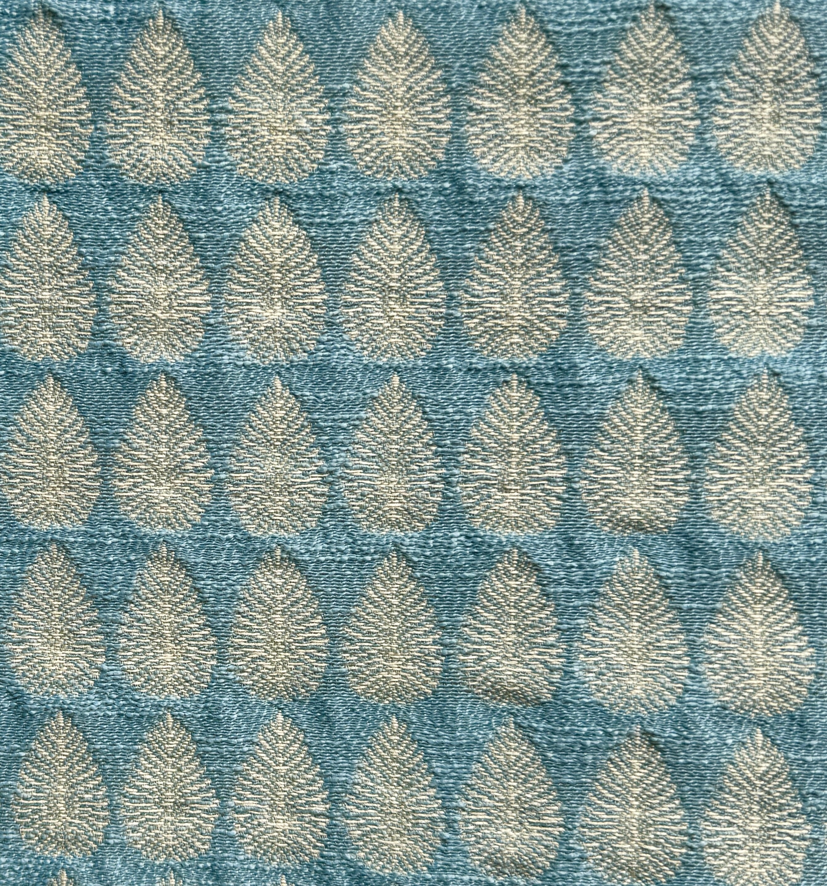 Detail of fabric woven in a repeating leaf print in shades of blue and gold.