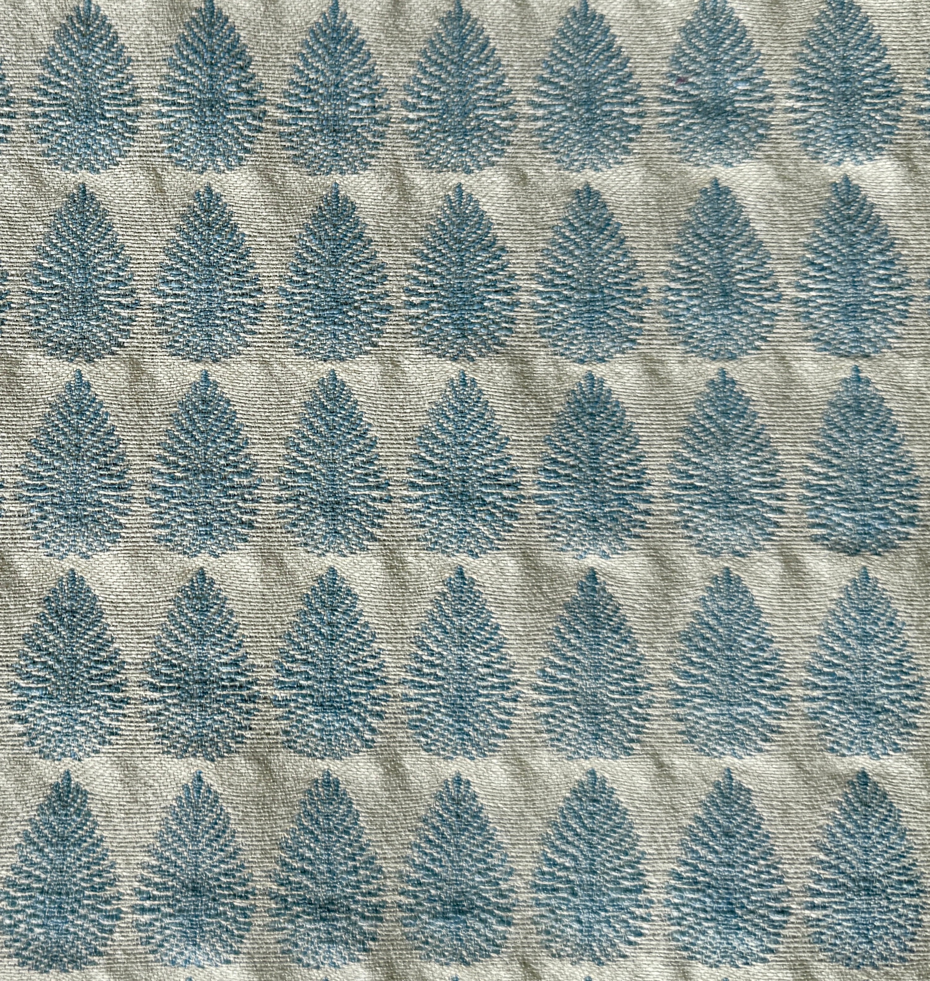 Detail of fabric woven in a repeating leaf print in shades of blue and gold.