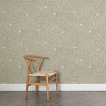 A wooden chair stands in front of a wall papered in a playful bird and leaf print in white on a sage field.