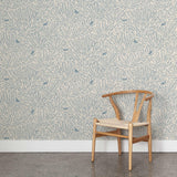 A wooden chair stands in front of a wall papered in a playful bird and leaf print in blue on a white field.