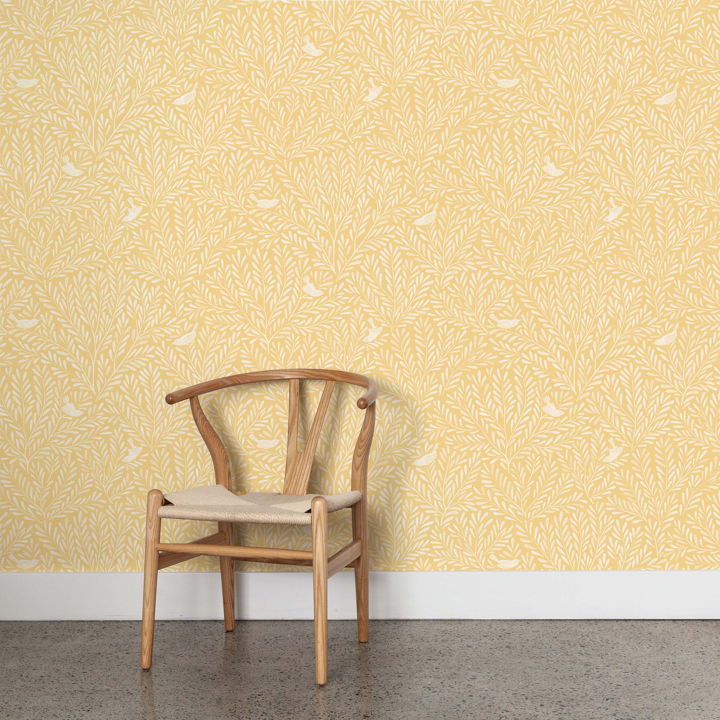 A wooden chair stands in front of a wall papered in a playful bird and leaf print in white on a yellow field.