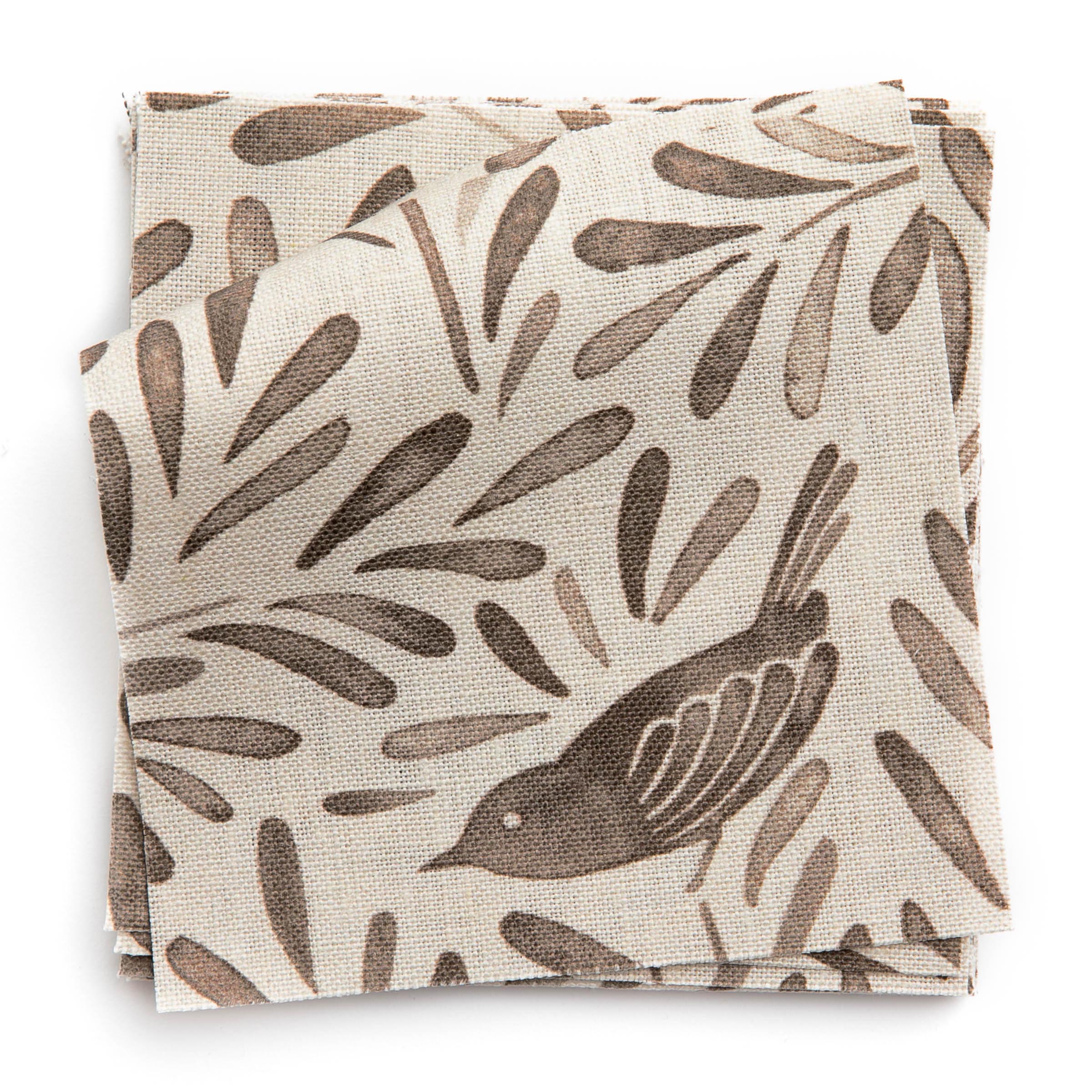 A stack of fabric swatches in a playful bird and leaf print in brown on a cream field.