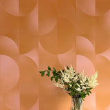 A vase of flowers stands in front of a wall covered in an abstract curvilinear print in mottled orange and pink.