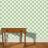 A wooden end table stands in front of a floral damask print in green on a cream field.