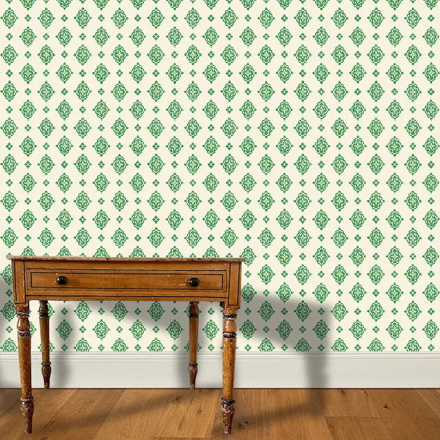 A wooden end table stands in front of a floral damask print in green on a cream field.