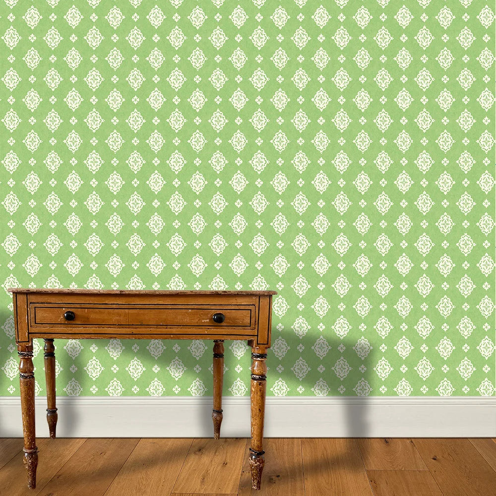 A wooden end table stands in front of a floral damask print in white on a green field.