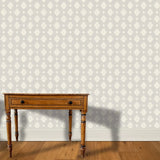 A wooden end table stands in front of a floral damask print in white on a light gray field.