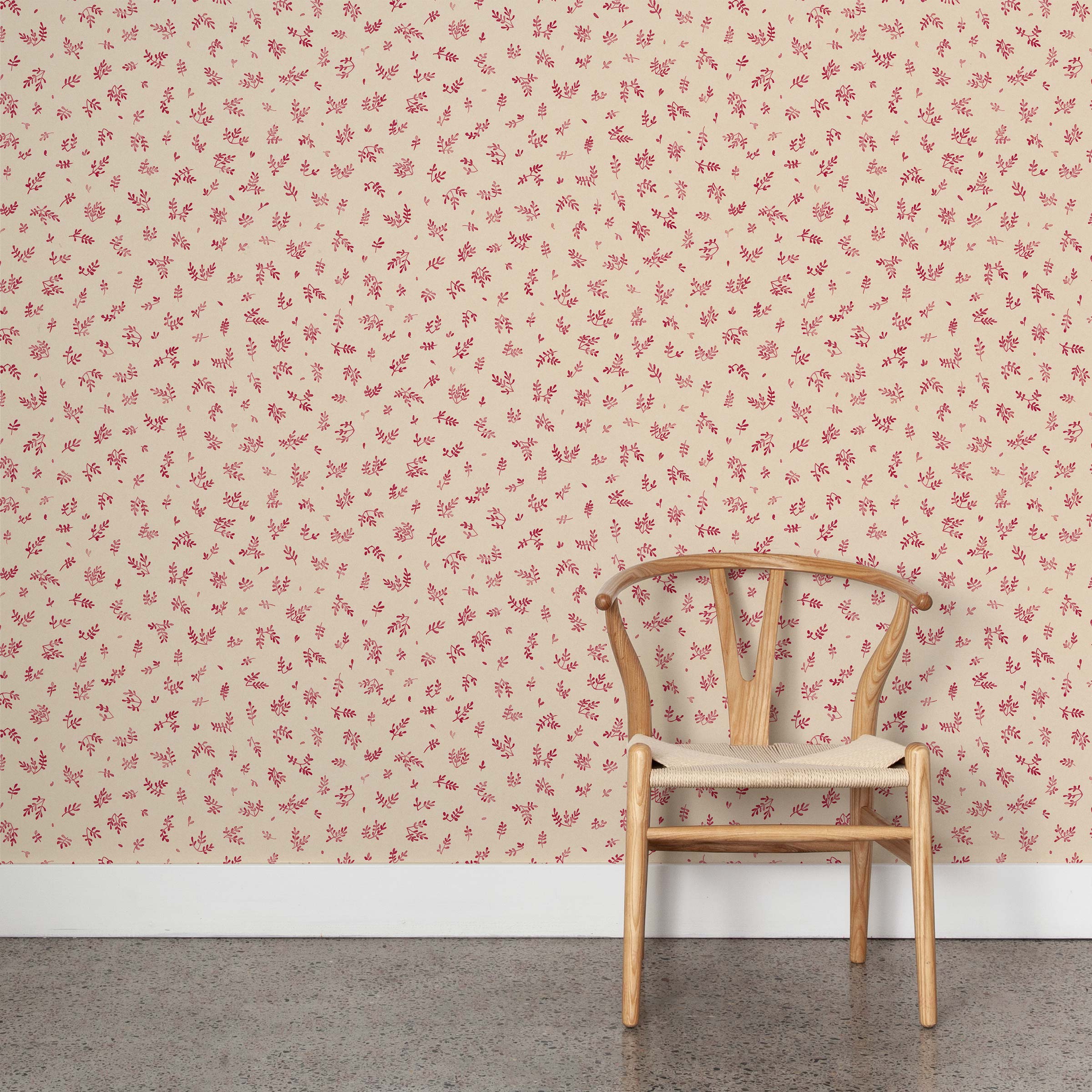 A wooden chair stands in front of a wall papered in a minimal repeating leaf print in pink on a tan field.