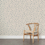 A wooden chair stands in front of a wall papered in a minimal repeating leaf print in navy on a cream field.