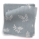 A stack of fabric swatches in a minimal repeating leaf print in cream on a blue-gray field.