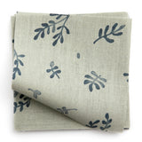 A stack of fabric swatches in a minimal repeating leaf print in navy on a light green field.