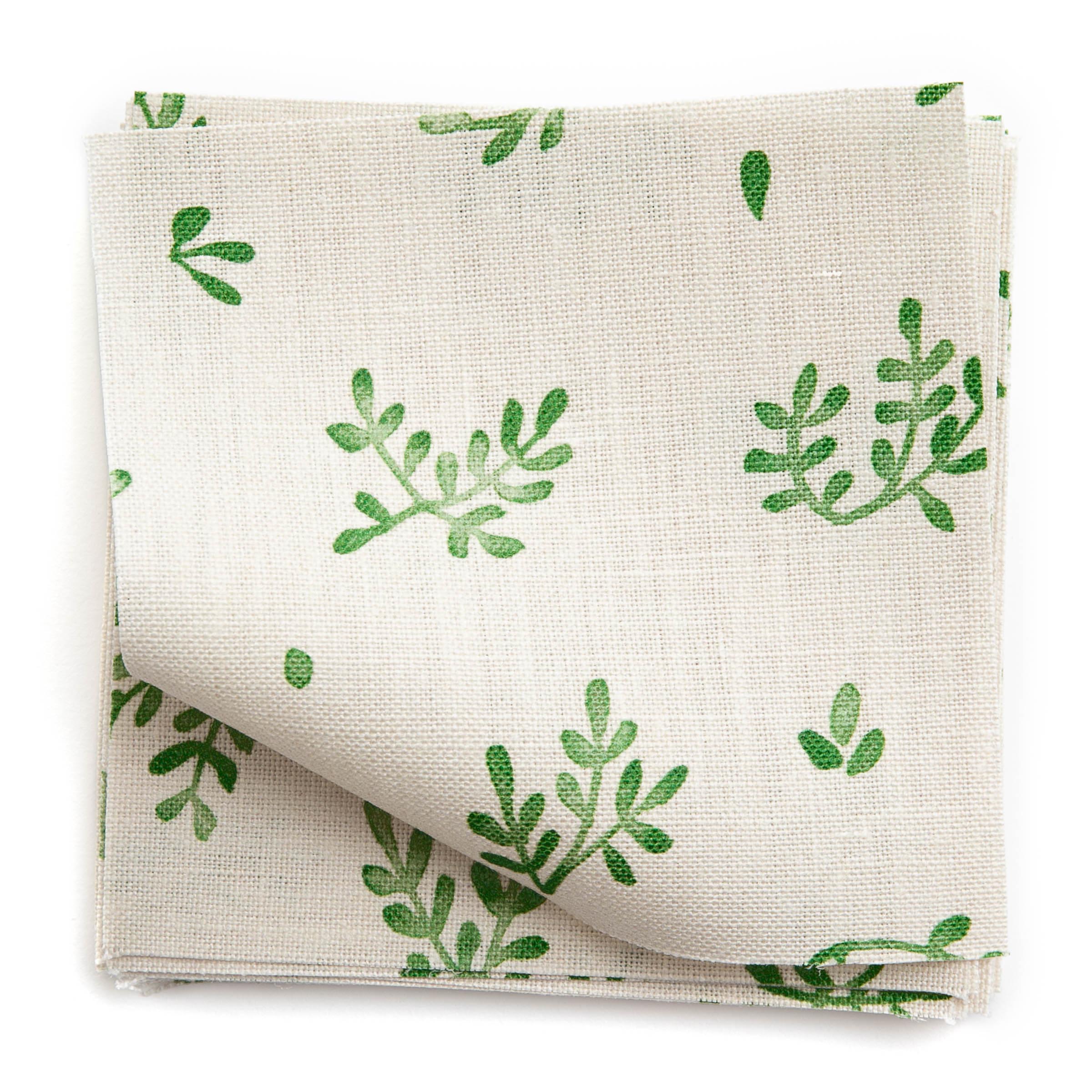 A stack of fabric swatches in a minimal repeating leaf print in green on a white field.