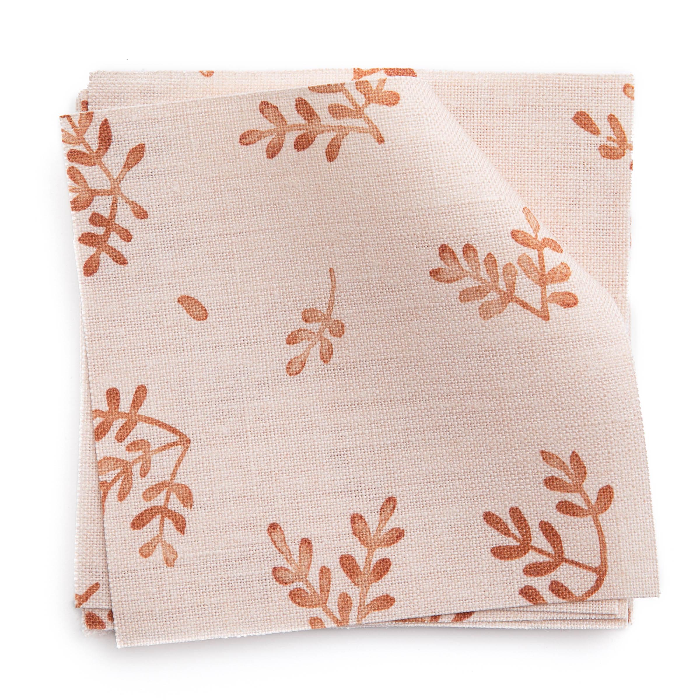 A stack of fabric swatches in a minimal repeating leaf print in red on a light pink field.