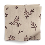 A stack of fabric swatches in a minimal repeating leaf print in brown on a tan field.