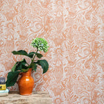 A vase of flowers stands in front of a wall papered in a playful squirrel and sunflower print in coral on a white field.