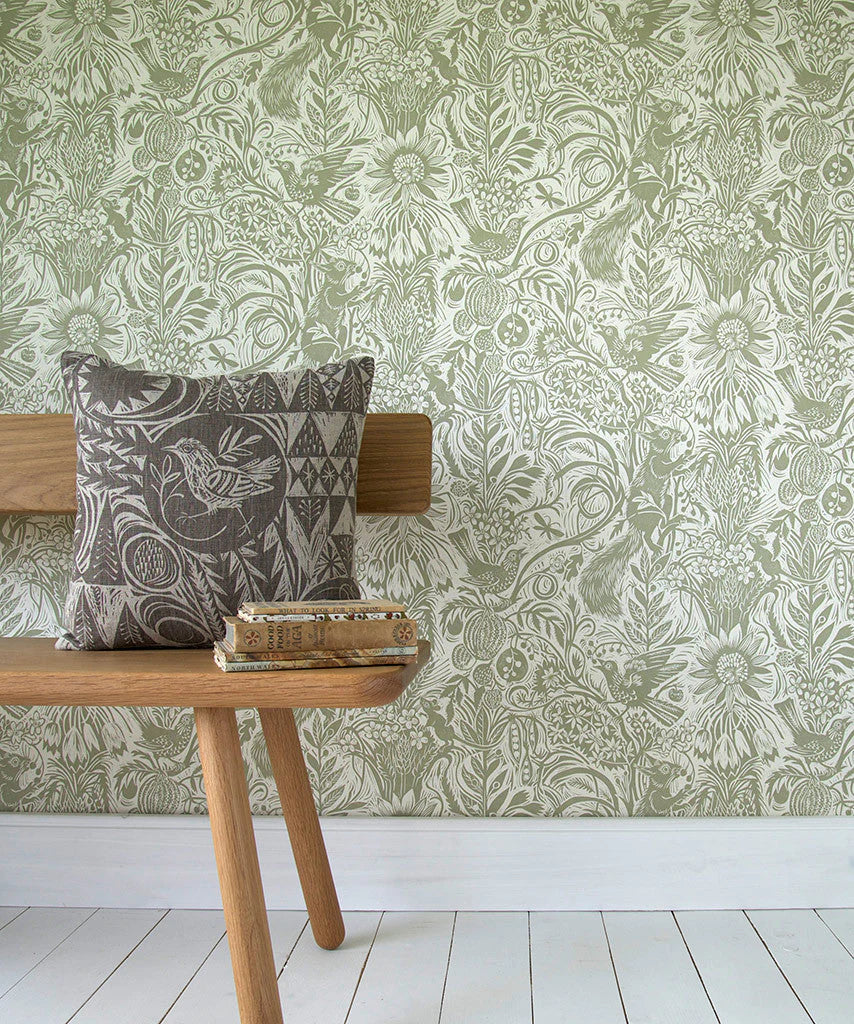 A wooden bench stands in front of a wall papered in a playful squirrel and sunflower print in sage on a cream field.