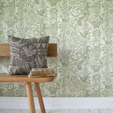 A wooden bench stands in front of a wall papered in a playful squirrel and sunflower print in sage on a cream field.